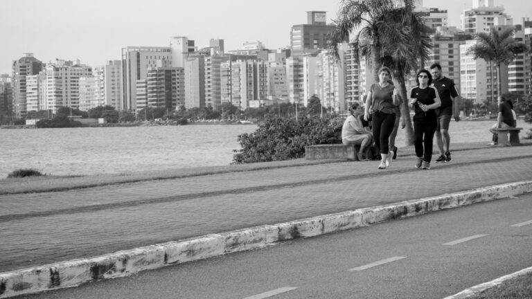 Um Grupo De Pessoas Caminhando Por Uma Rua Ao Lado De Um Corpo Dagua MHD3m5DSBDc
