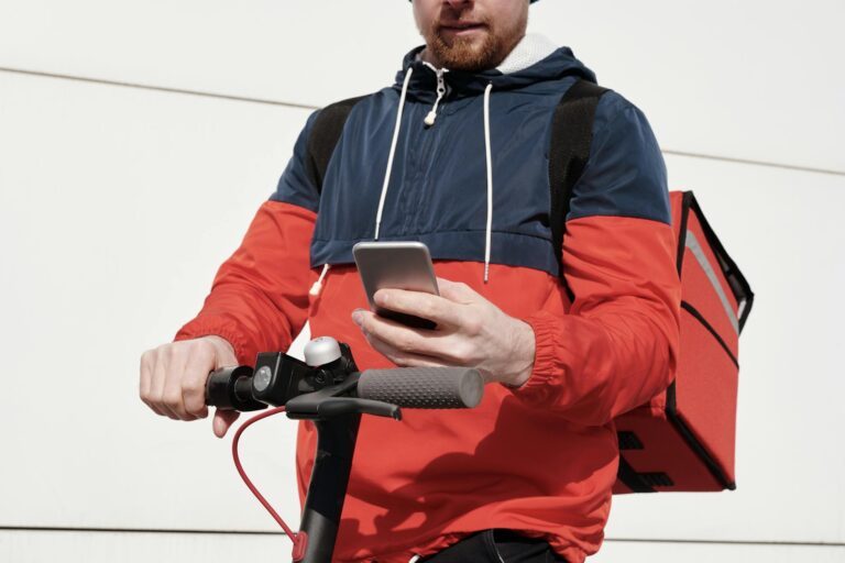 Delivery worker checks phone while riding scooter. Urban logistics concept.
