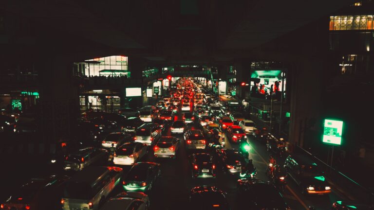 Dynamic night scene of heavy traffic on a city road with bright lights and illuminated buildings surrounding the area.