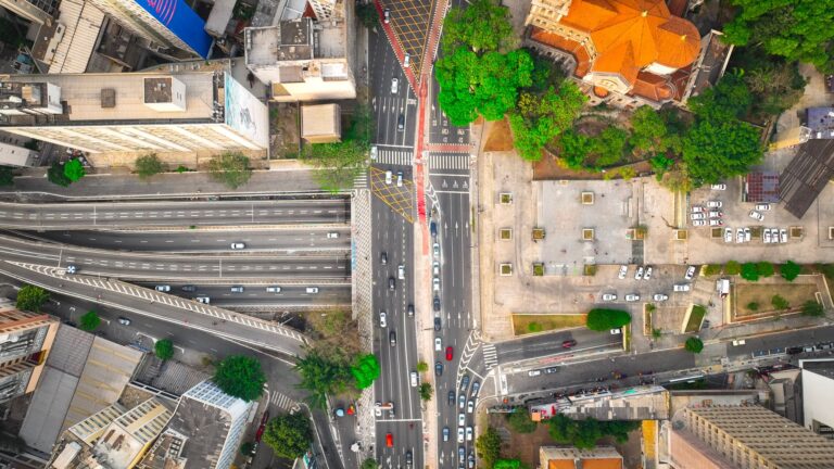 A dynamic aerial shot of a city intersection with lush greenery and buildings.