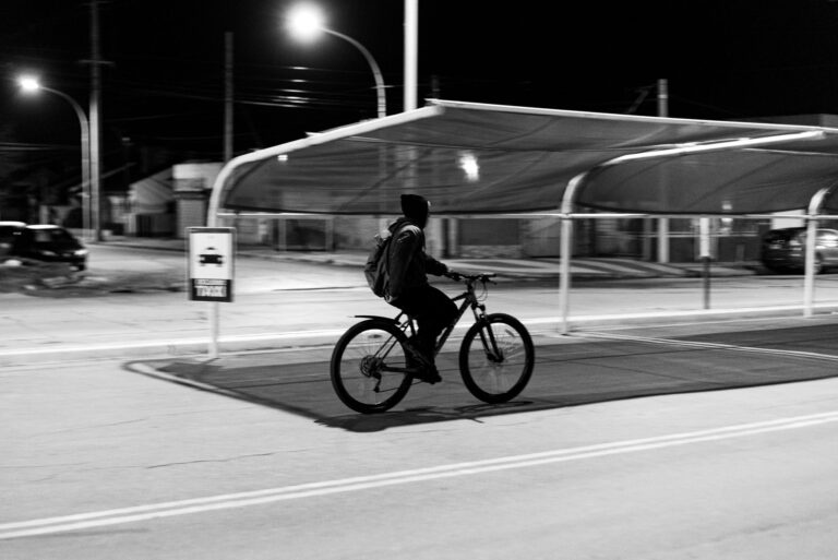 A cyclist rides through the streets of Bahía Blanca, Argentina at night in a black and white scene.